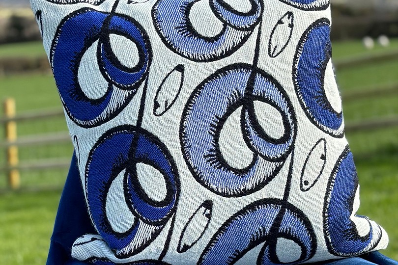 Y Ddafad Gorniog 45cm cushion in Electric blue, black and ecru, displayed on a chair